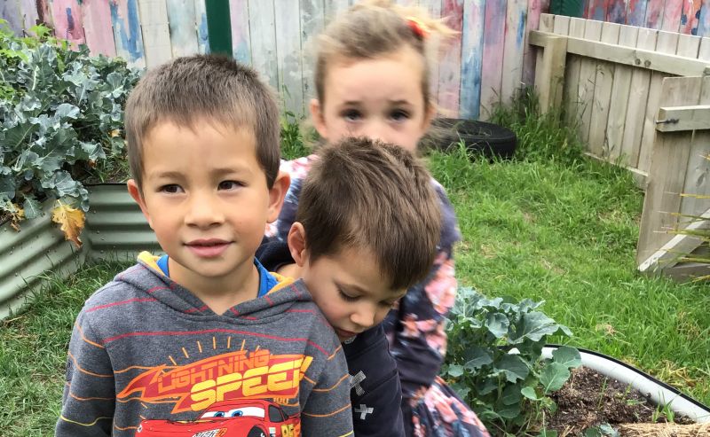 Three children standing in vegetable garden.