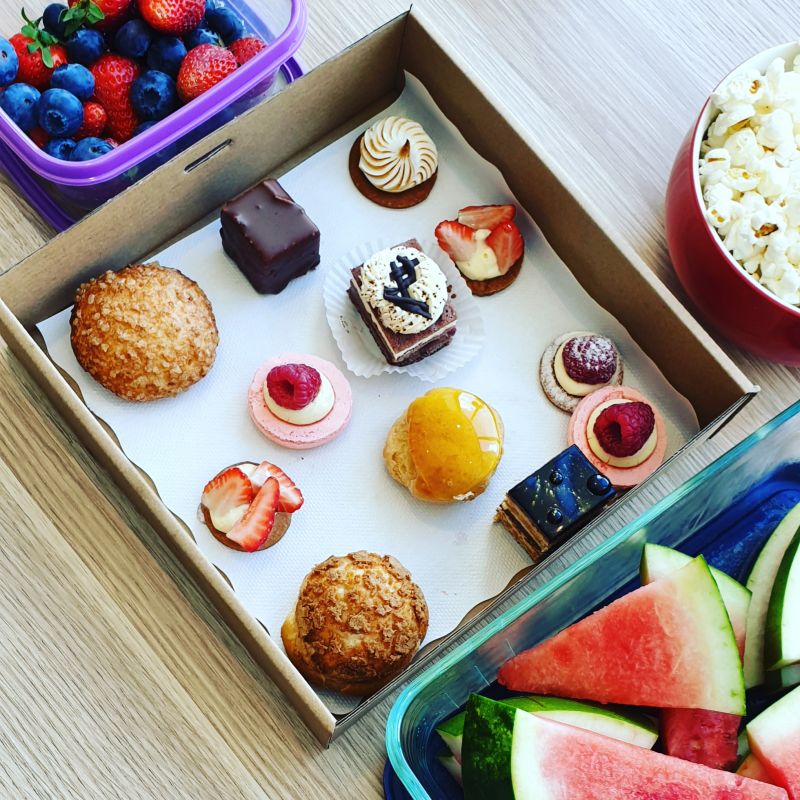 Selection of  deserts in a box, with fruit and popcorn in surrounding containers.