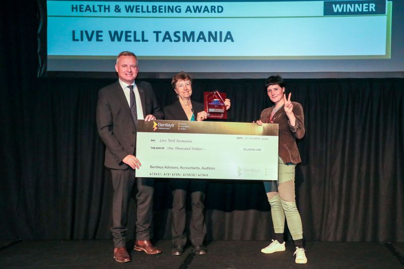 Winners of the Healthy Tasmania Health and Wellbeing Award for the Tasmanian Community Achievement Awards. On stage holding the cheque is Premier and Minister for Mental Health and Wellbeing Jeremy Rockliff with Live Well Tasmania members. Robin Krabbe, centered, is holding up the award. 
